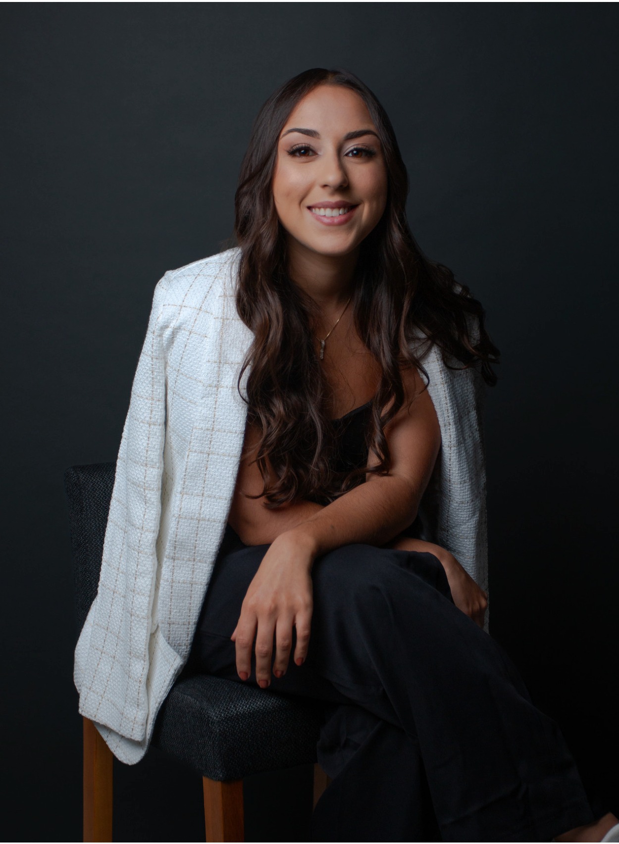 Retrato corporativo de advogada com blazer branco em fundo escuro